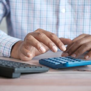 person using calculator at desk with coffee mug